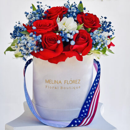 Pure white box with American flag ribbon, accompanied by red roses, white astromelias and blue Baby Breath.