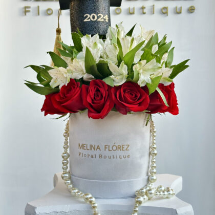 Small white velvet box with a beautiful pearl arrangement in red roses and white astromelias. accompanied by a black cap with gold, is the most desired among graduates.