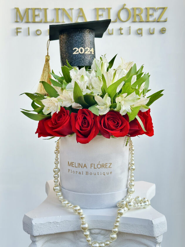 Small white velvet box with a beautiful pearl arrangement in red roses and white astromelias. accompanied by a black cap with gold, is the most desired among graduates.