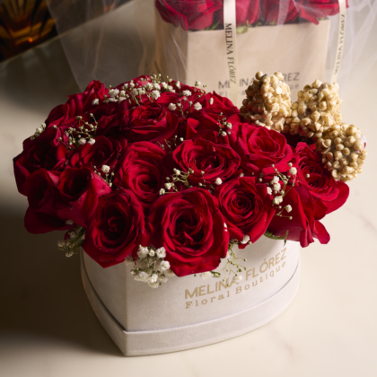 White heart in red roses and baby breath accompanied by three strawberries covered in white chocolate, chips and gold dust.